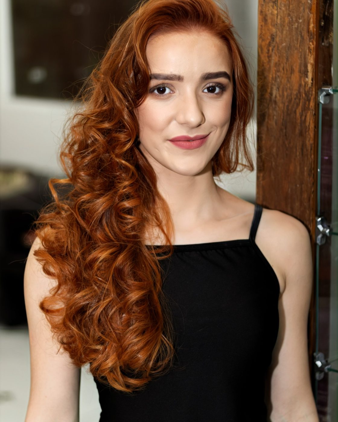 Modelo ruiva com cachos longos no salão, encostada em pilar de madeira