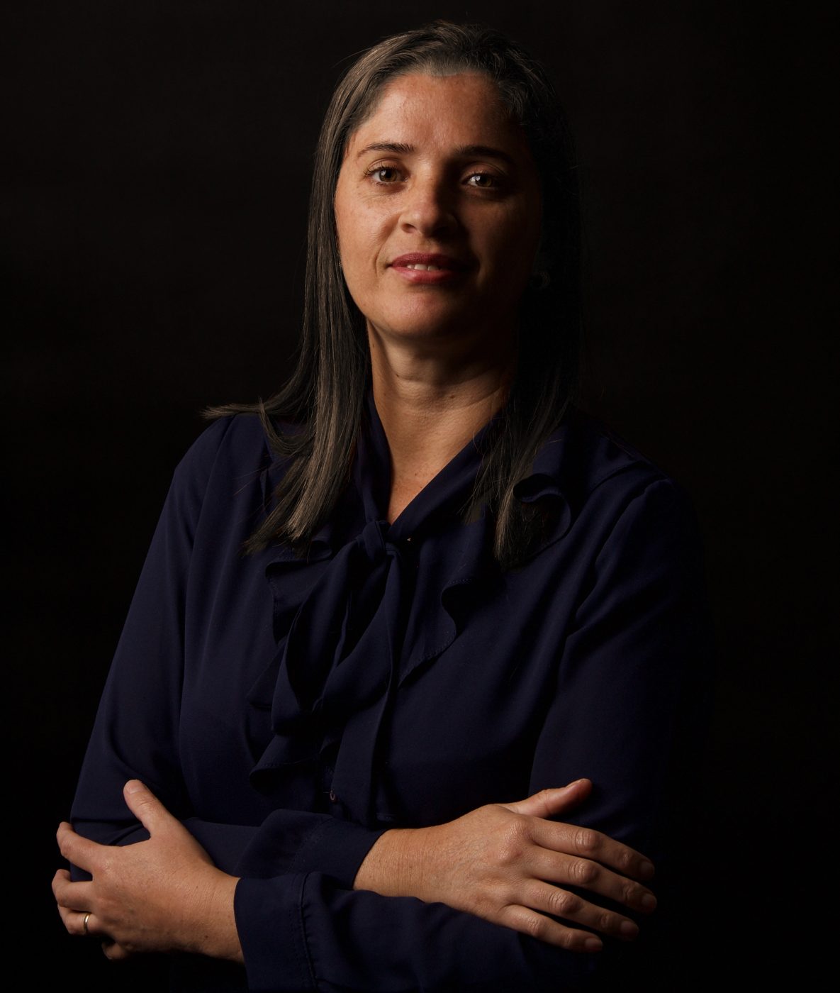 Retrato corporativo de mulher de braços cruzados em fundo preto
