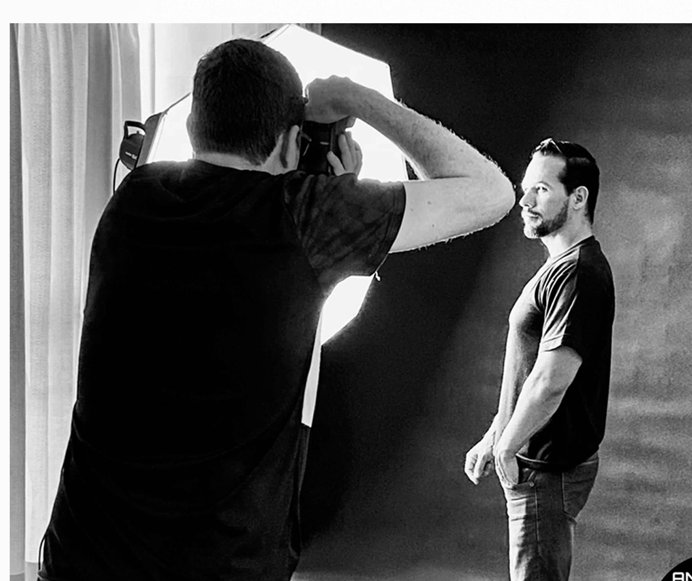 Bastidores em estúdio: fotógrafo com softbox fotografando modelo em fundo cinza, preto e branco