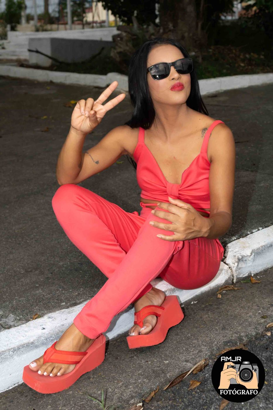 Modelo com conjunto coral e óculos escuros sentada no meio-fio